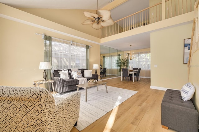 living room with light wood-style floors, baseboards, high vaulted ceiling, and ceiling fan with notable chandelier