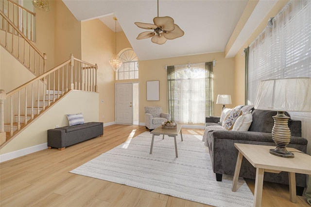 living room featuring baseboards, wood finished floors, stairs, high vaulted ceiling, and ceiling fan with notable chandelier