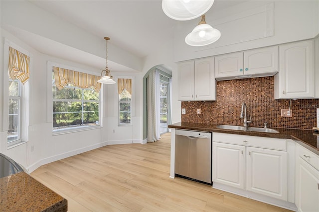 kitchen featuring arched walkways, light wood-style flooring, backsplash, stainless steel dishwasher, and a sink