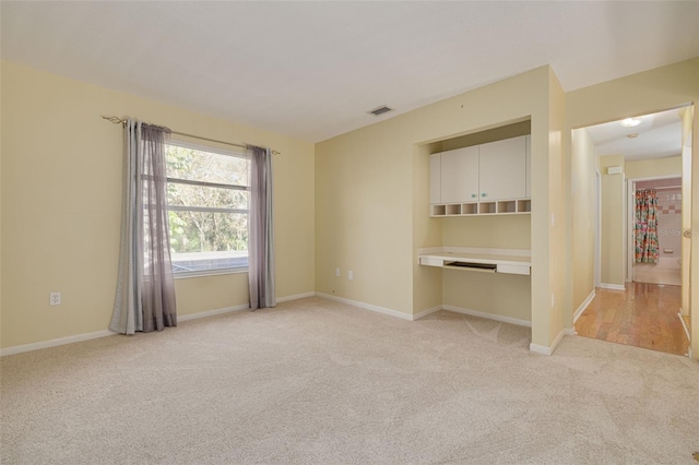 spare room featuring light carpet, visible vents, baseboards, and built in study area