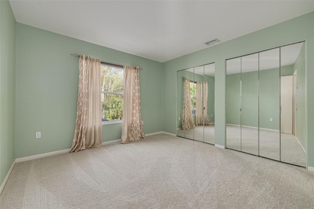 unfurnished bedroom featuring multiple windows, carpet flooring, two closets, and visible vents