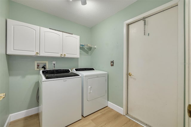 clothes washing area with a textured ceiling, light wood-style flooring, separate washer and dryer, baseboards, and cabinet space