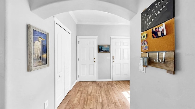 hall with light wood-style floors, arched walkways, ornamental molding, and baseboards
