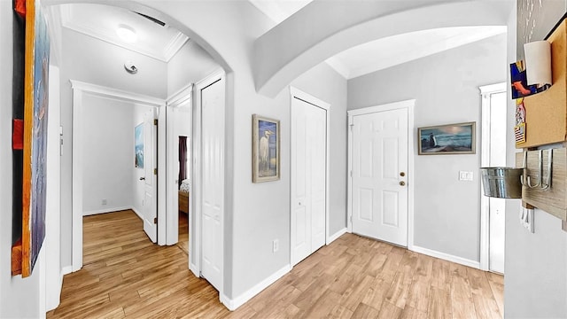 hall with arched walkways, crown molding, baseboards, and light wood-style floors