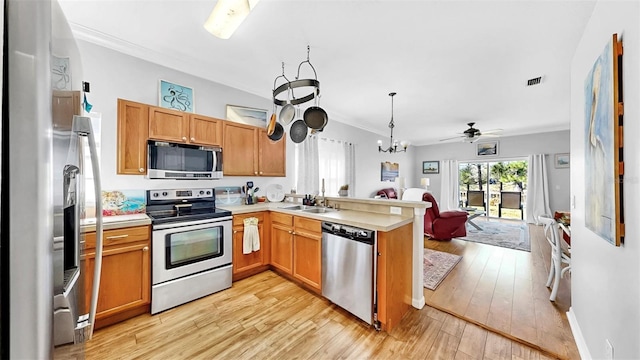 kitchen with appliances with stainless steel finishes, open floor plan, a peninsula, light wood-style floors, and a sink