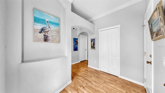 corridor featuring baseboards, arched walkways, wood finished floors, and ornamental molding