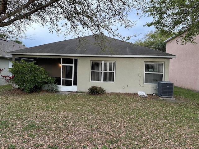 back of house featuring a lawn, a sunroom, roof with shingles, central air condition unit, and stucco siding