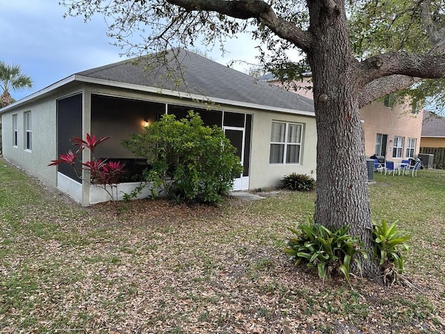 exterior space featuring a yard, roof with shingles, a sunroom, and stucco siding