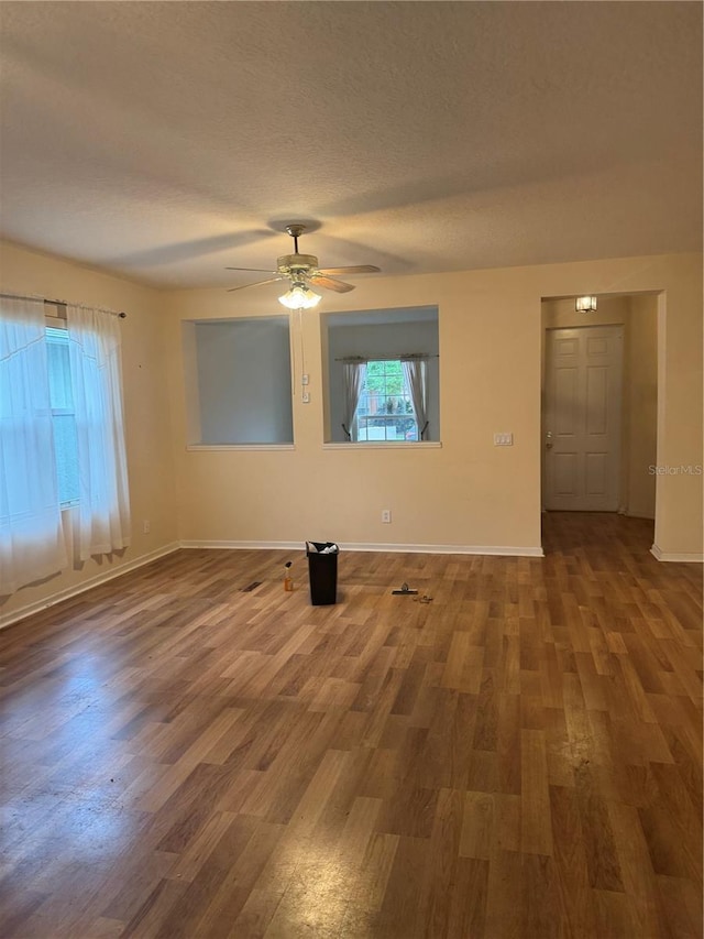 unfurnished room with a textured ceiling, ceiling fan, wood finished floors, and baseboards