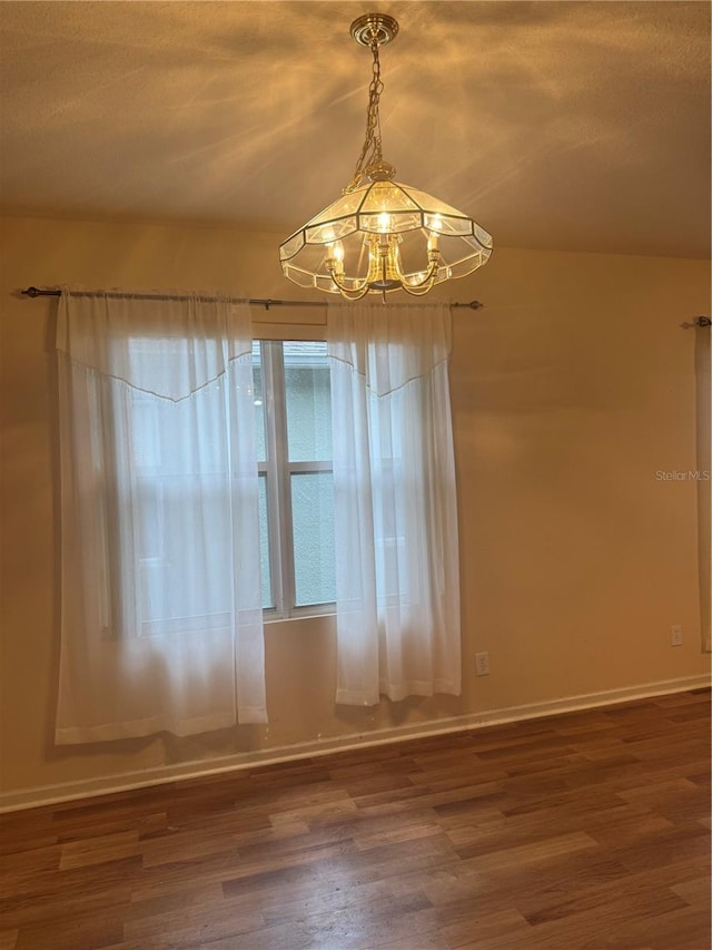spare room with a notable chandelier, a textured ceiling, wood finished floors, and baseboards