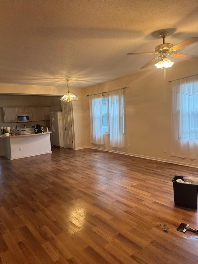 unfurnished living room with a textured ceiling, baseboards, dark wood-style flooring, and ceiling fan with notable chandelier