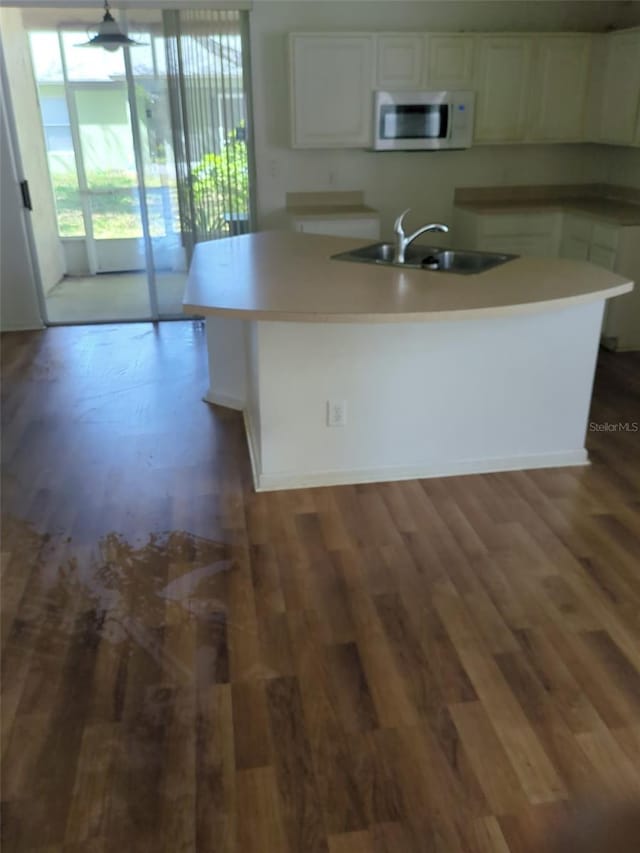 kitchen featuring wood finished floors, a sink, white cabinetry, light countertops, and an island with sink