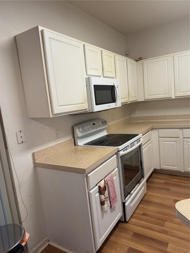 kitchen with light wood finished floors, light countertops, white appliances, and white cabinetry