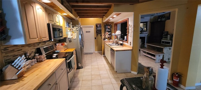 kitchen featuring wood counters, tasteful backsplash, appliances with stainless steel finishes, light tile patterned floors, and baseboards