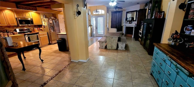 kitchen featuring a ceiling fan, light tile patterned flooring, a fireplace, stainless steel appliances, and decorative backsplash