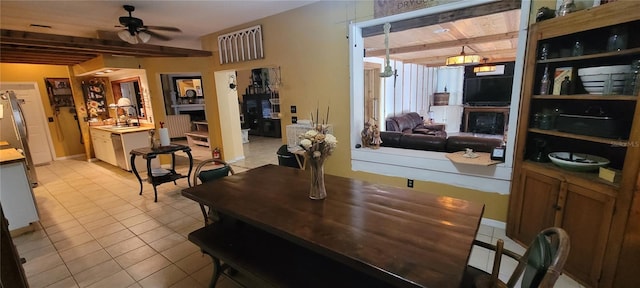 dining room featuring beam ceiling, light tile patterned floors, a fireplace, and a ceiling fan