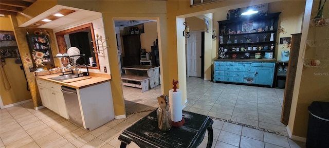 kitchen featuring light tile patterned floors, wood counters, stainless steel dishwasher, and a sink