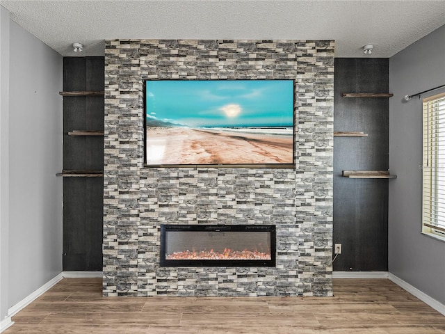 unfurnished living room featuring a textured ceiling, baseboards, wood finished floors, and a stone fireplace