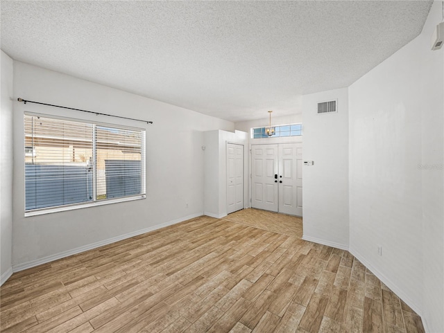 spare room featuring a textured ceiling, baseboards, visible vents, and light wood-style floors