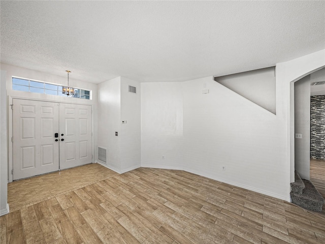 foyer entrance featuring a textured ceiling, a notable chandelier, wood finished floors, visible vents, and baseboards