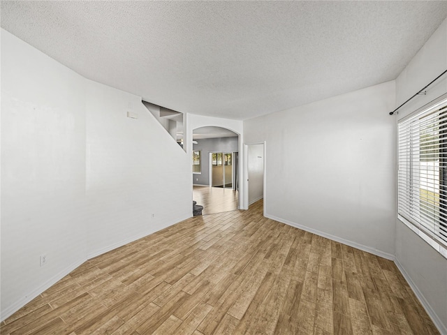 empty room featuring baseboards, a textured ceiling, arched walkways, and wood finished floors