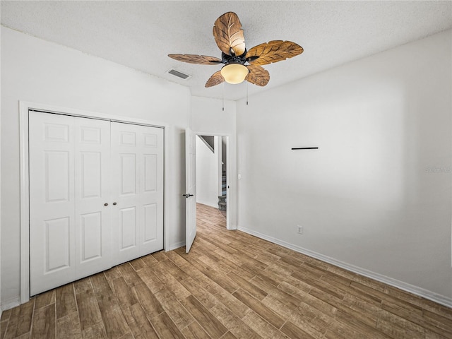 unfurnished bedroom featuring a closet, visible vents, a textured ceiling, and wood finished floors