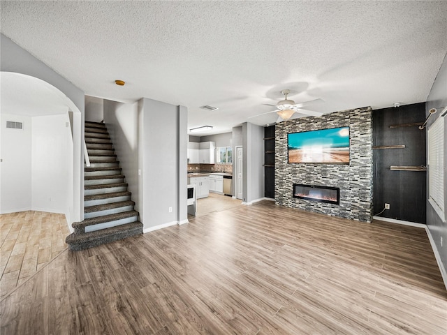 unfurnished living room featuring visible vents, stairway, light wood-style floors, a ceiling fan, and a large fireplace