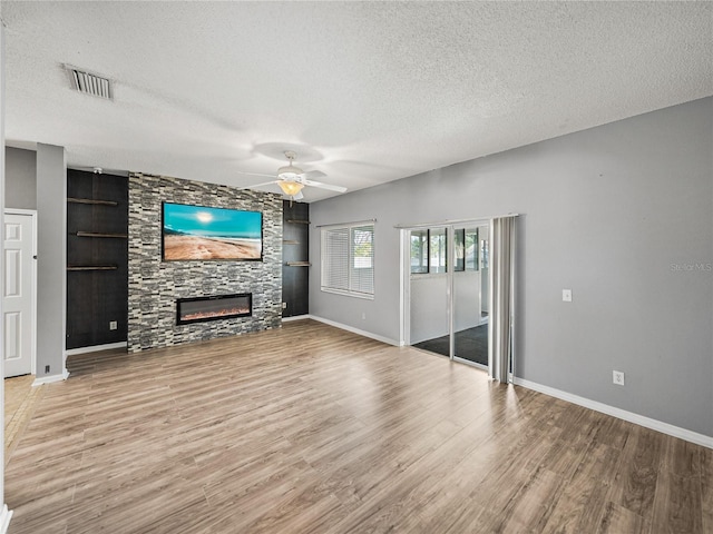 unfurnished living room featuring visible vents, wood finished floors, a textured ceiling, built in shelves, and a fireplace