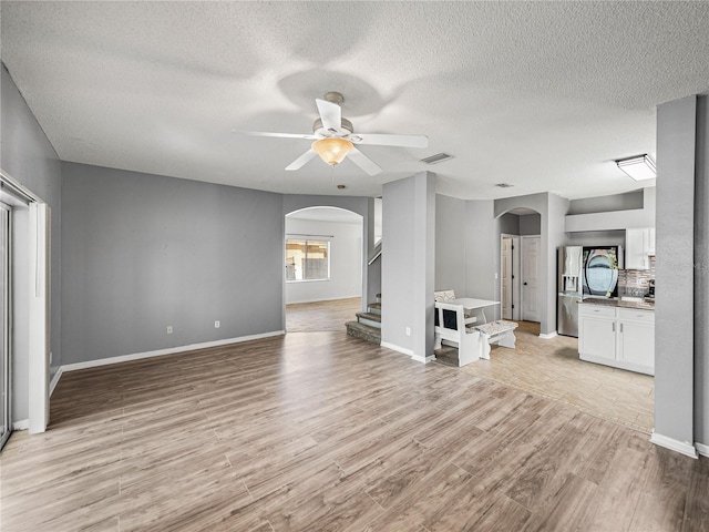 unfurnished living room featuring arched walkways, visible vents, ceiling fan, light wood-type flooring, and stairs