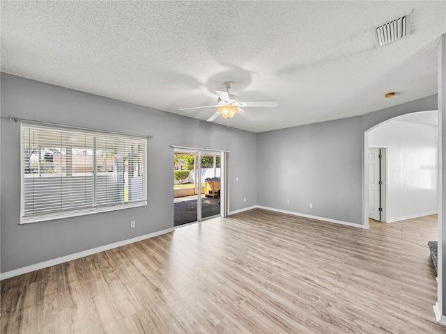 empty room featuring arched walkways, light wood finished floors, visible vents, ceiling fan, and baseboards