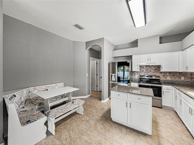 kitchen with arched walkways, white cabinets, decorative backsplash, a kitchen island, and appliances with stainless steel finishes