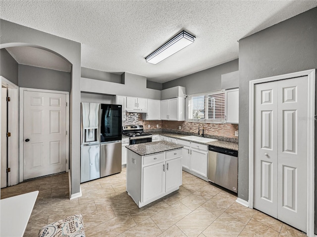 kitchen with arched walkways, white cabinets, a center island, stainless steel appliances, and a sink