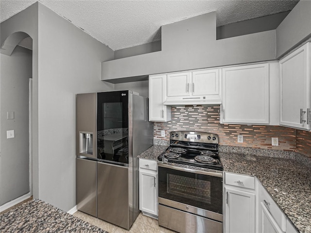 kitchen featuring under cabinet range hood, white cabinetry, appliances with stainless steel finishes, dark stone counters, and tasteful backsplash