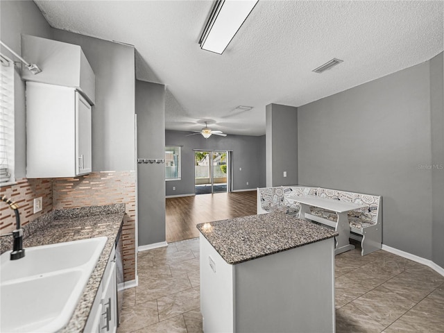 kitchen featuring visible vents, white cabinets, open floor plan, a center island, and a sink