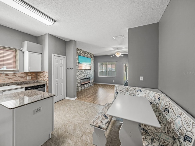 kitchen featuring white cabinets, ceiling fan, open floor plan, a stone fireplace, and backsplash