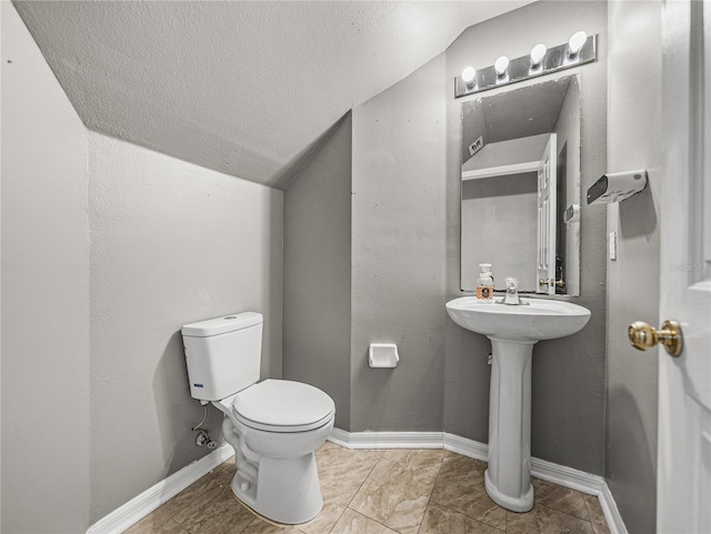 bathroom featuring toilet, a textured wall, baseboards, and lofted ceiling