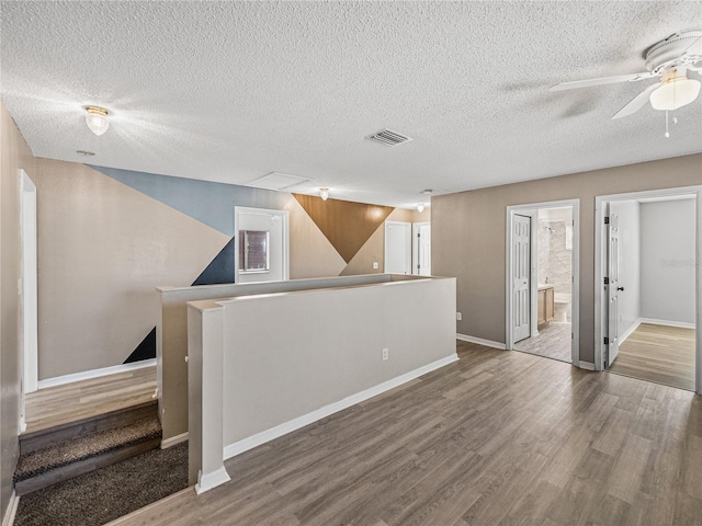 empty room featuring a textured ceiling, wood finished floors, visible vents, and baseboards