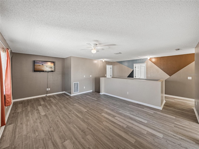 unfurnished living room with a textured ceiling, wood finished floors, a ceiling fan, visible vents, and baseboards