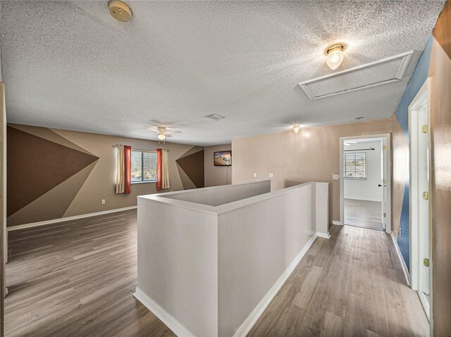 hall featuring a textured ceiling, wood finished floors, an upstairs landing, baseboards, and attic access