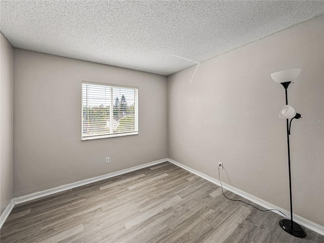 spare room with a textured ceiling, baseboards, and wood finished floors