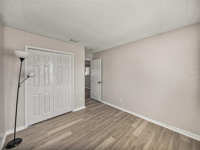 unfurnished bedroom with baseboards, a closet, visible vents, and wood finished floors