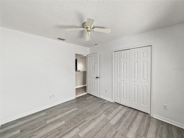 unfurnished bedroom with a closet, visible vents, a textured ceiling, wood finished floors, and baseboards