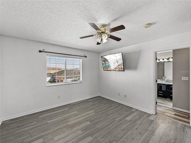 unfurnished bedroom featuring a textured ceiling, ensuite bathroom, wood finished floors, a ceiling fan, and baseboards