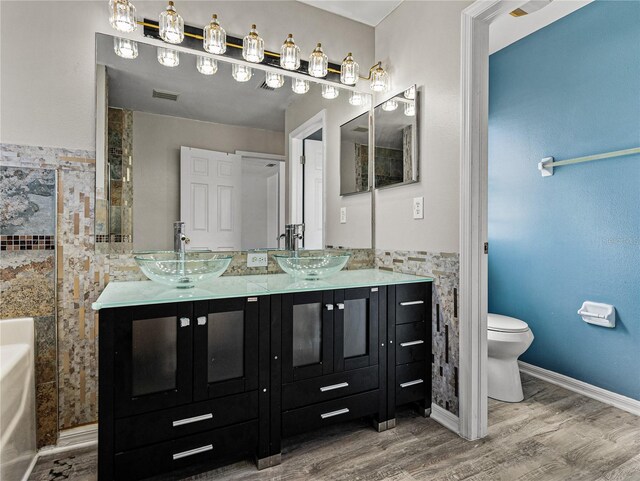 bathroom with visible vents, tile walls, a sink, and wood finished floors