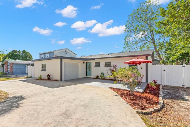 view of front of house with concrete driveway, an attached garage, a gate, fence, and stucco siding