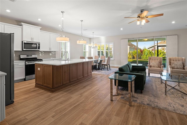 kitchen with stainless steel appliances, light countertops, light wood-style flooring, open floor plan, and a sink