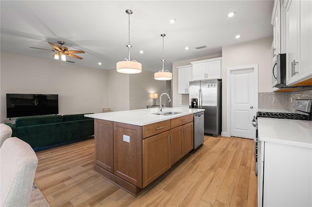 kitchen featuring stainless steel appliances, open floor plan, a kitchen island with sink, white cabinetry, and a sink