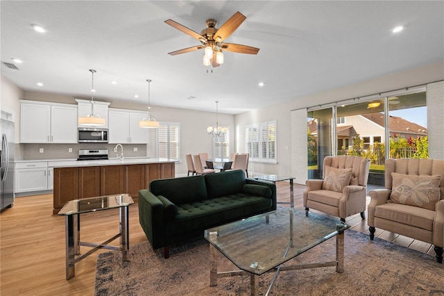 living area featuring light wood finished floors, ceiling fan with notable chandelier, visible vents, and recessed lighting