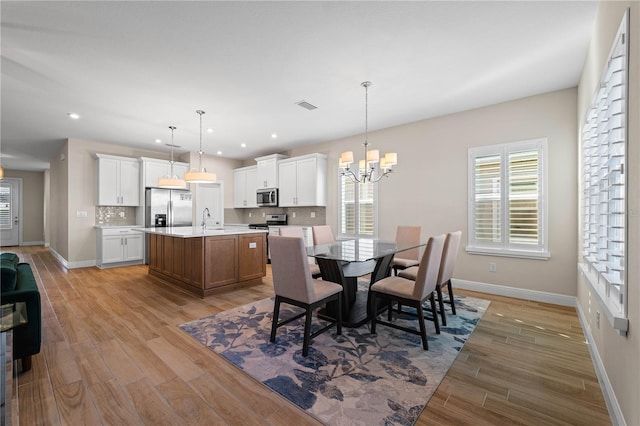 dining space with light wood finished floors, baseboards, visible vents, and a notable chandelier