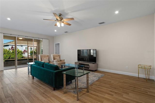 living area featuring a ceiling fan, visible vents, baseboards, and wood finished floors